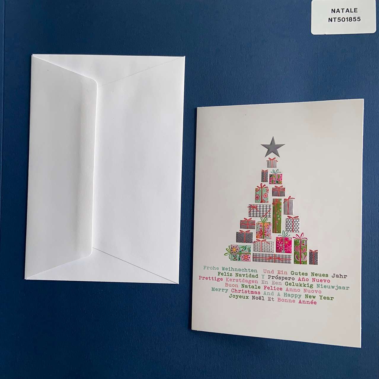 Biglietto di Natale personalizzabile con un testo nell'anta interna. In copertina un albero di natale formato da tanti piccoli pacchi regalo e alla base auguri di natale in tutte le lingue e in colori diversi